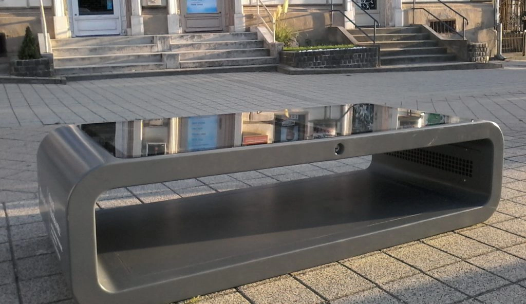 Grey custom branded Kuube Nano solar smart bench with integrated solar panel in public space