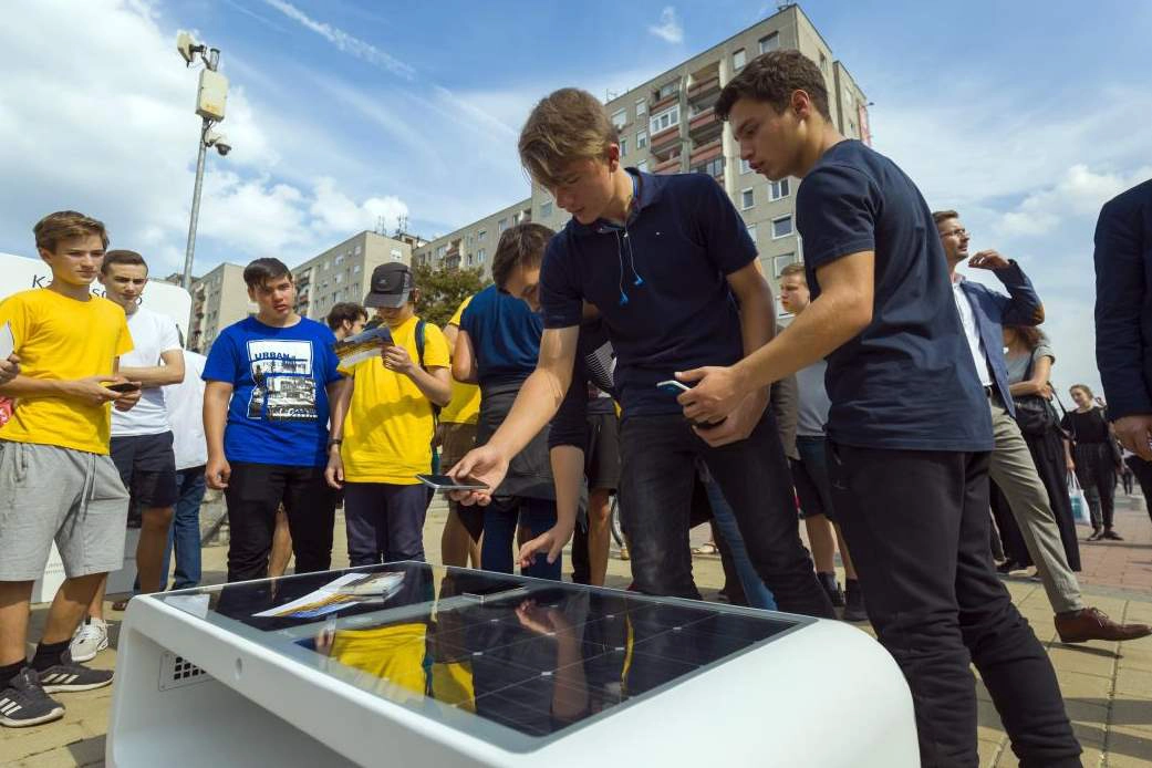 People using Kuube Nano solar smart bench with integrated solar panels in urban public space