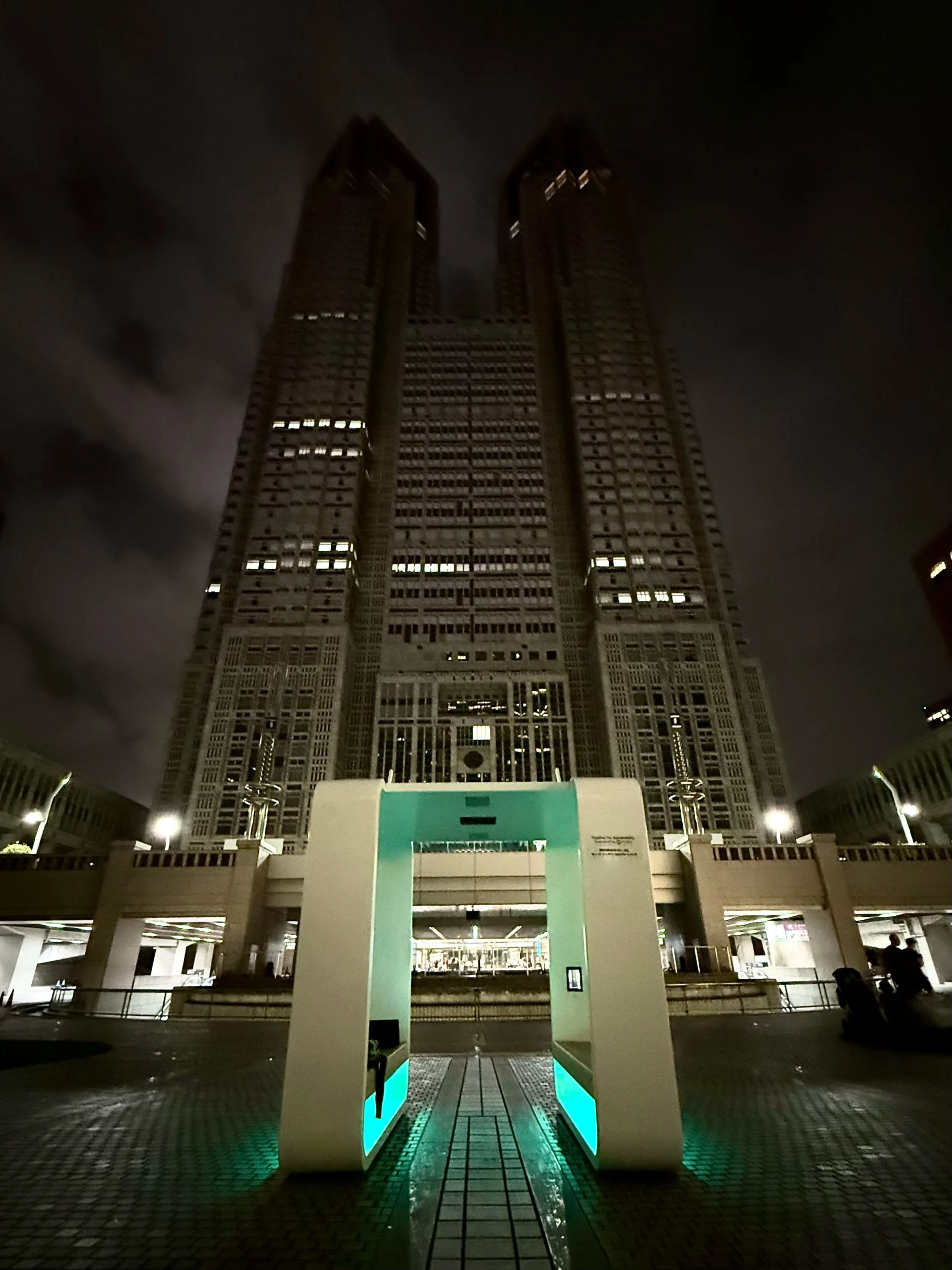 Night view of the Tokyo Metropolitan Government Building in Shinjuku with a glowing smart city bench installation in the foreground.